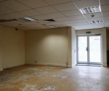 Vacant retail unit with exposed floor wear, dated ceiling tiles, and an unrefreshed customer entry before turnover work